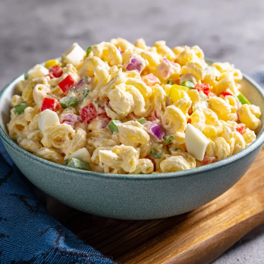A vibrant classic macaroni salad recipe with colorful vegetables in a teal bowl.