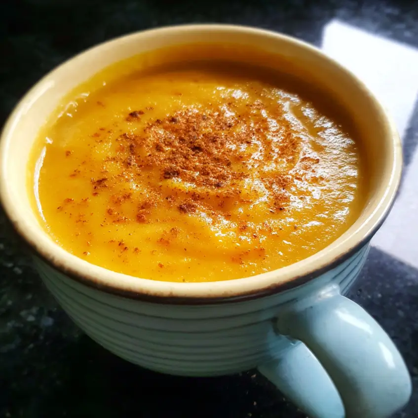 A warm mug of creamy sweet potato soup, garnished with spices, resting on a dark countertop.