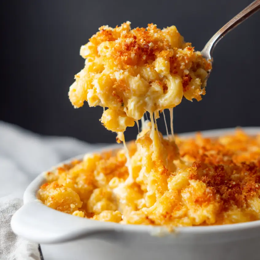 Close-up of a spoon lifting creamy, baked macaroni and cheese with a golden-brown crispy topping and a delicious cheese pull, perfect for a Christmas mac and cheese recipe.