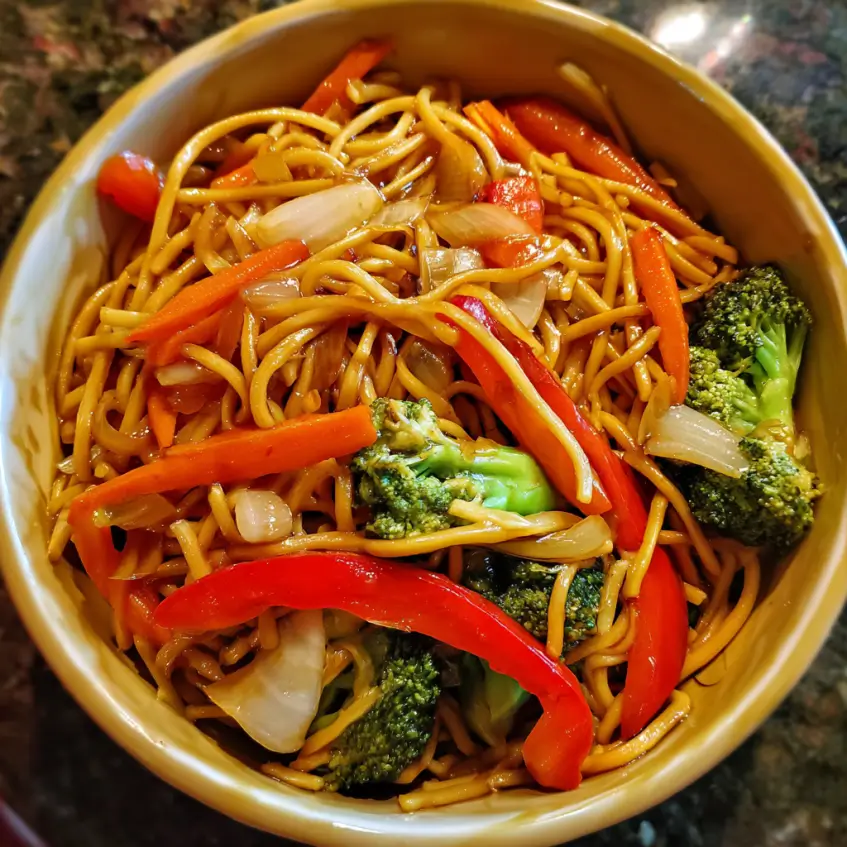 A vibrant bowl of Easy Vegetable Lo Mein with colorful carrots, red bell peppers, and broccoli on a dark surface.