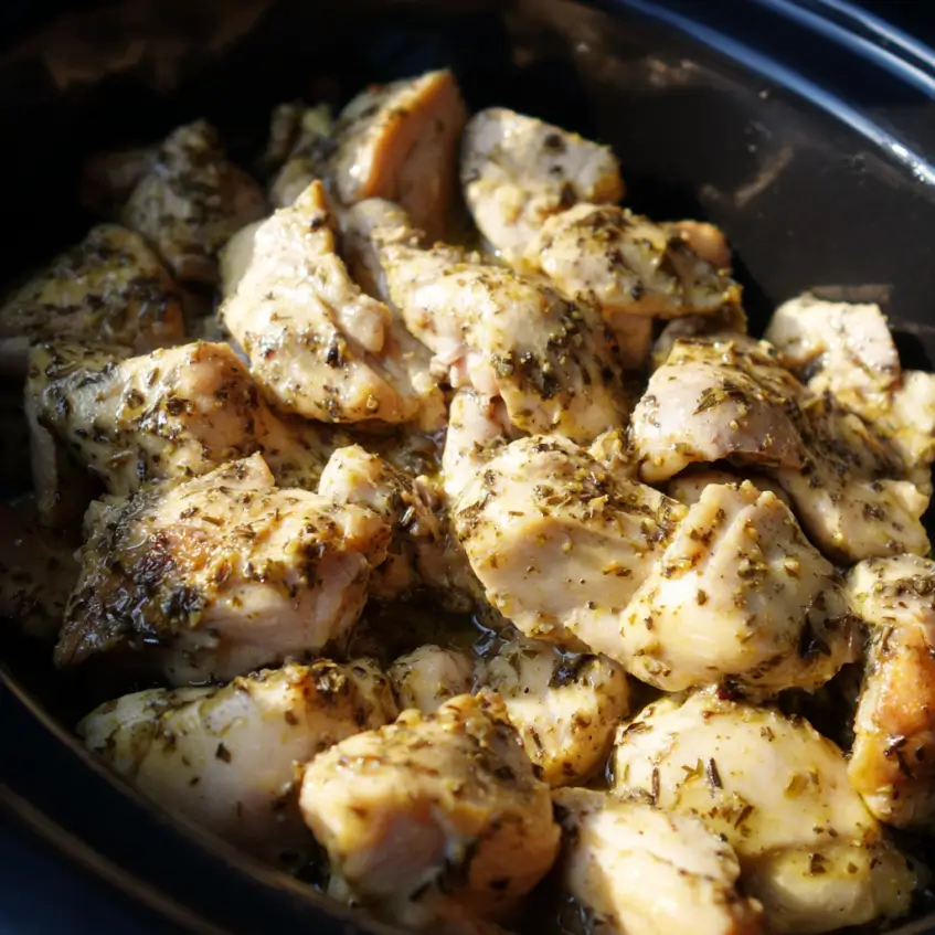 Close-up of seasoned, cooked chicken simmering in a dark crockpot, perfect for a frozen chicken crockpot recipe.