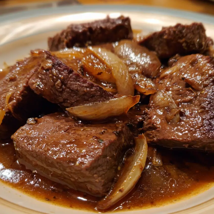 Close-up of tender beef chunks and caramelized onions in a rich sauce, ready from a delicious steak crockpot recipe.